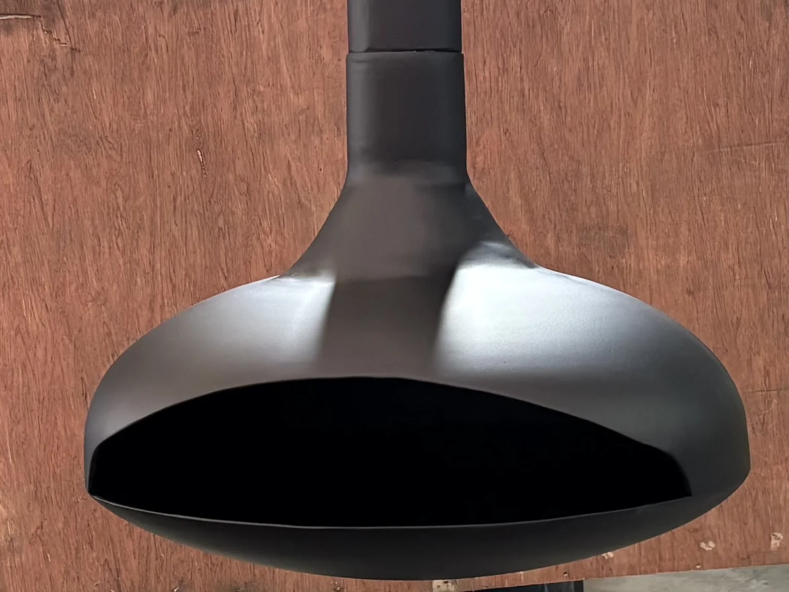 Campana metálica negra con acabado uniforme mate sobre fondo de madera.