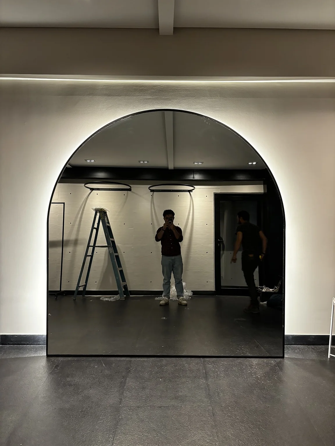 Espejo de gran formato con remate superior arqueado y retroiluminación perimetral, instalado en interior.