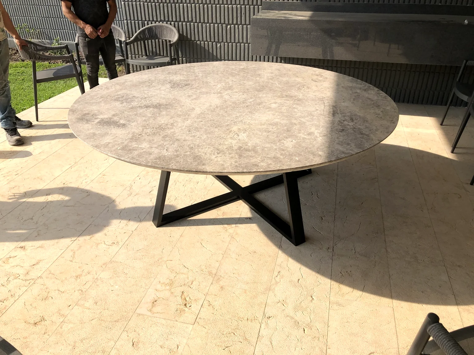 Mesa redonda de gran formato con cubierta tipo piedra y base metálica negra.